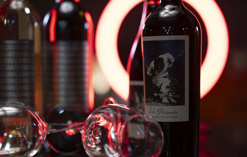 Image of a bottle of Prisoner wine and wine glasses in front of a red light